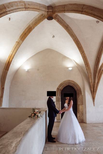 Nevěsta a ženich se drží za ruce v gotické síni