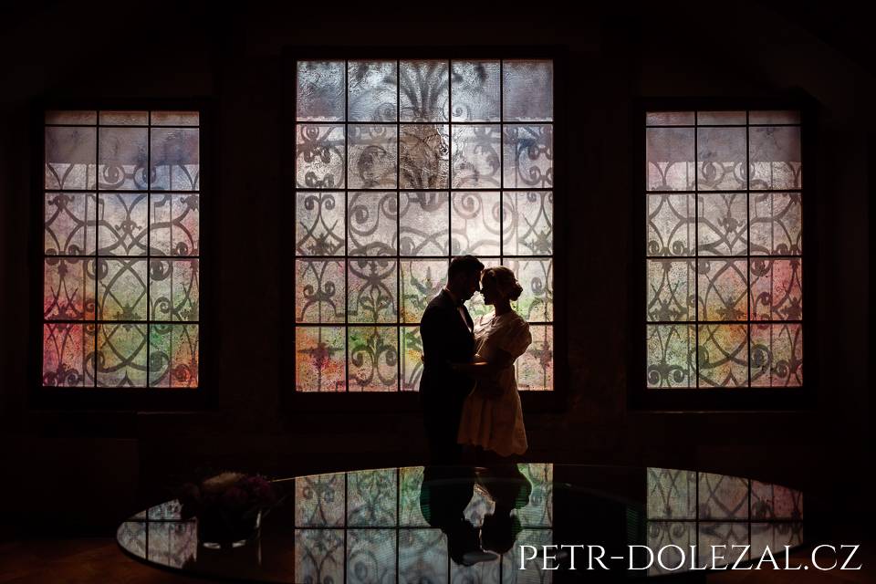 artistic photo with silhouettes of bride and groom in front of colourful window