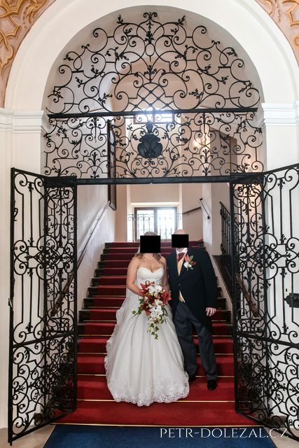 Bride and groom under stairs with red carpet in Brevnov Monastery