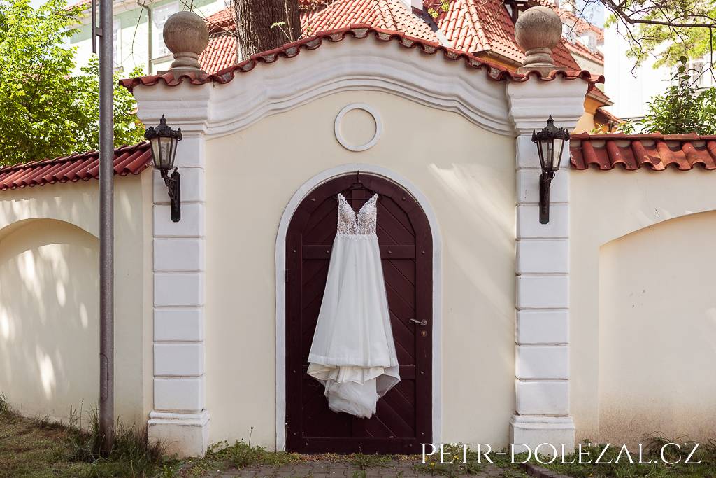 Svatební šaty pověšené na dveřích v areálu parkoviště před Altány Kampa