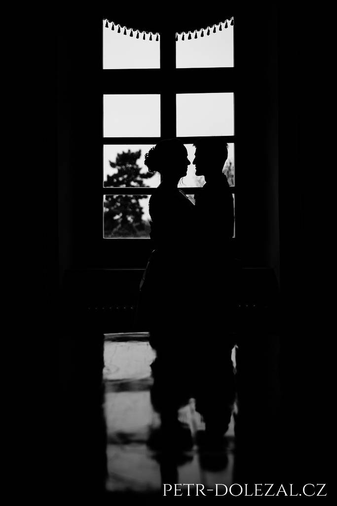 Siluety novomanželů před oknem na zámku Chvaly, zrcadlící se v desce stolu