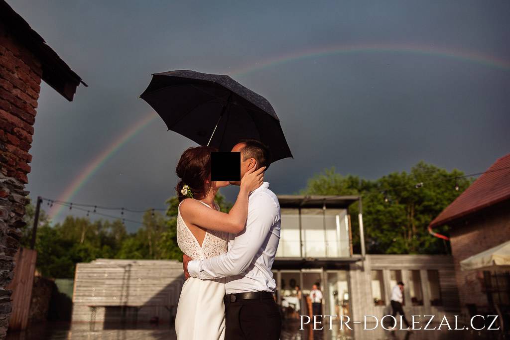 Polibek nevěsty a ženicha pod deštníkem a pod duhou