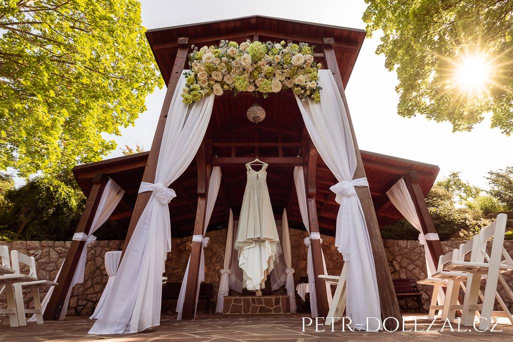 Šaty nevěsty pověšené v zahradním altánu Park Hotelu Popovičky
