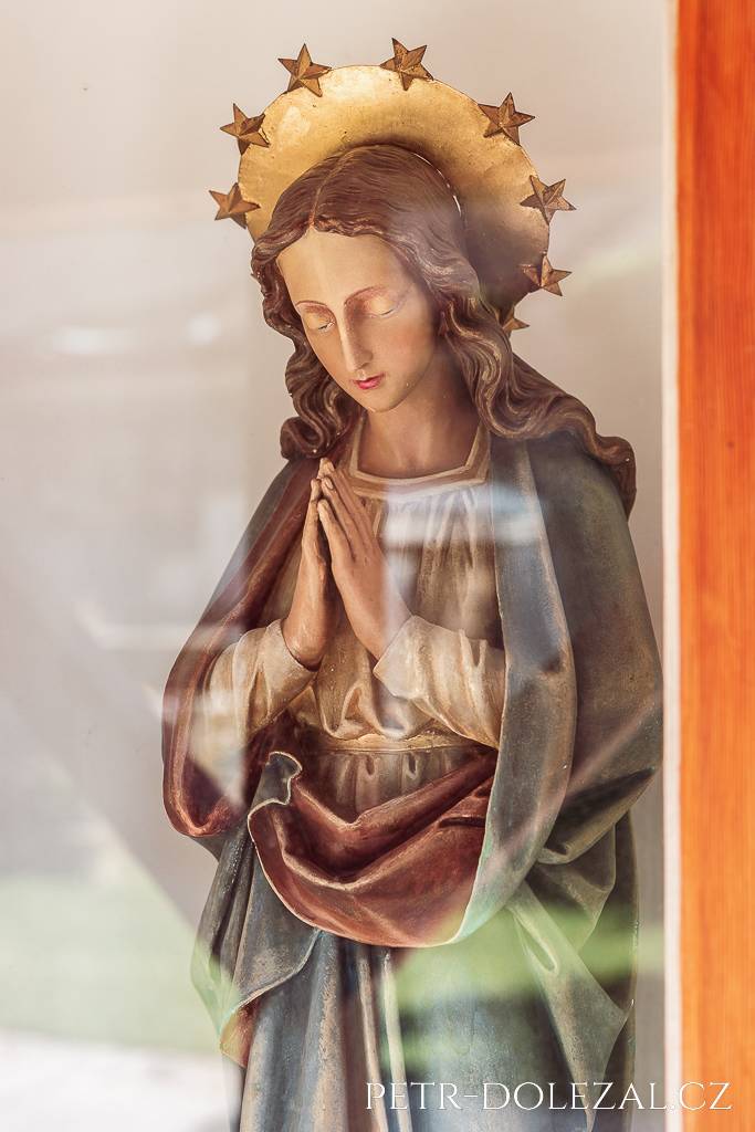 Soška Panny Marie zasklená ve zdi statku