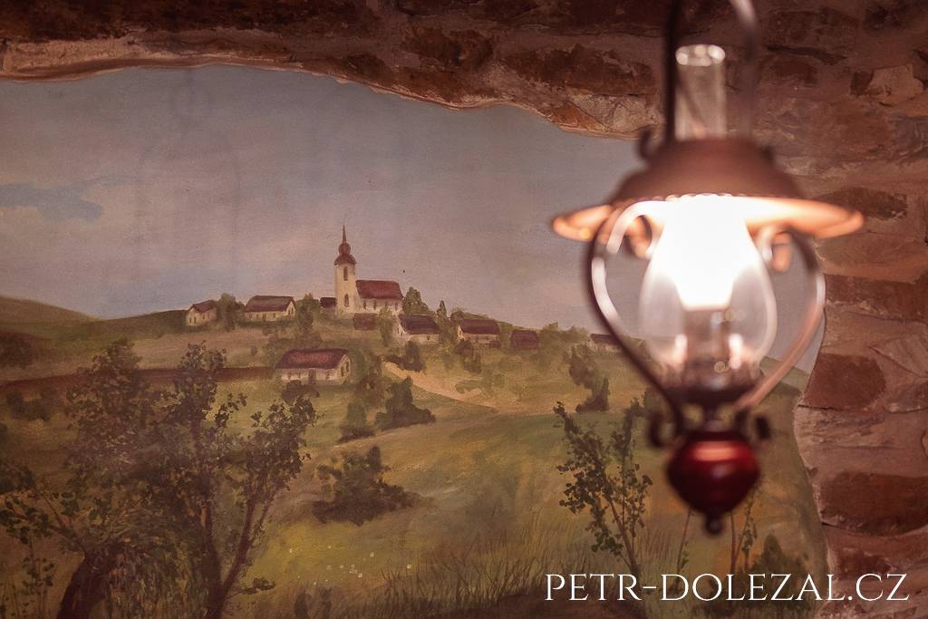 Nástěnná malba s domečky a kostelíkem vyfotografovaná uvnitř jedné z místností statku U Škodů