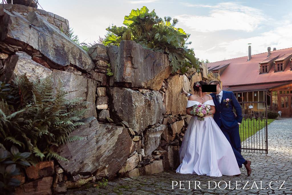 Nevěsta a ženich pózující u kamenné zídky na cestě k hotelu Všetice