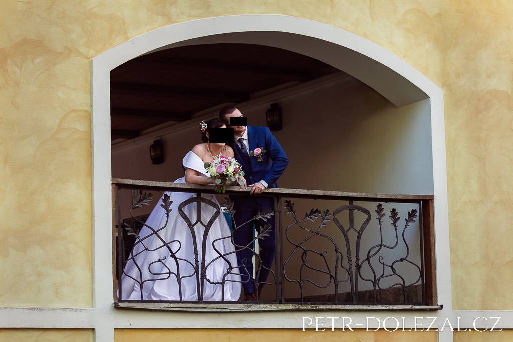 Nevěsta se ženichem vyhlížející přes ozdobné zábradlí od hotelu Všetice