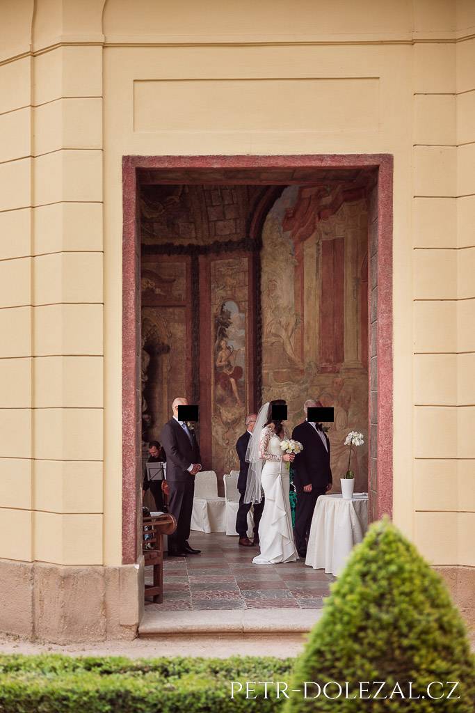Nevěsta, ženich a svědkové nastoupení v průběhu svatebního obřadu ve Vrtbovské zahradě, zarámovaní průchodem sala terreny