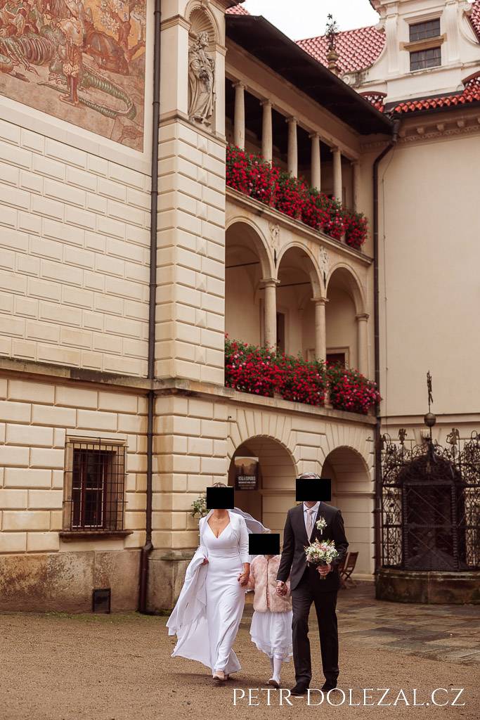 Nevěsta, dcera a ženich kráčející po nádvoří Průhonického zámku