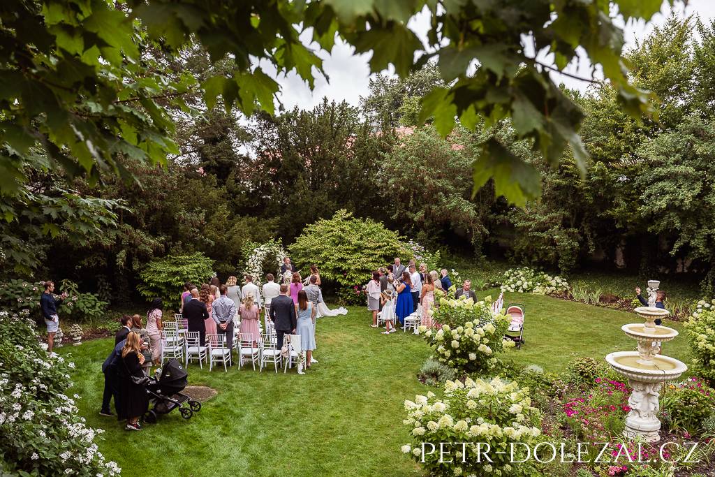 Probíhající svatební obřad se stojícími svatebčany v zahradě zámku Trnová