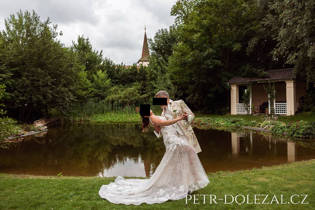 Nevěsta a ženich pózují na břehu rybníčku u zámku Trnová