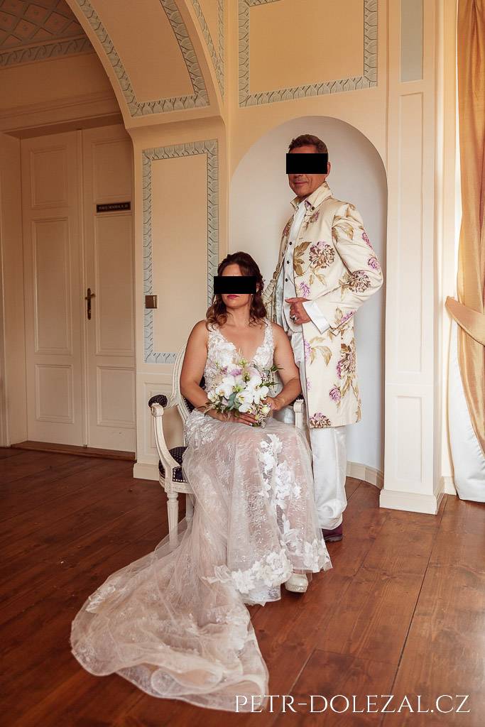Nevěsta sedící na historickém křesle, ženich stojící za ní, interiér zámku Trnová