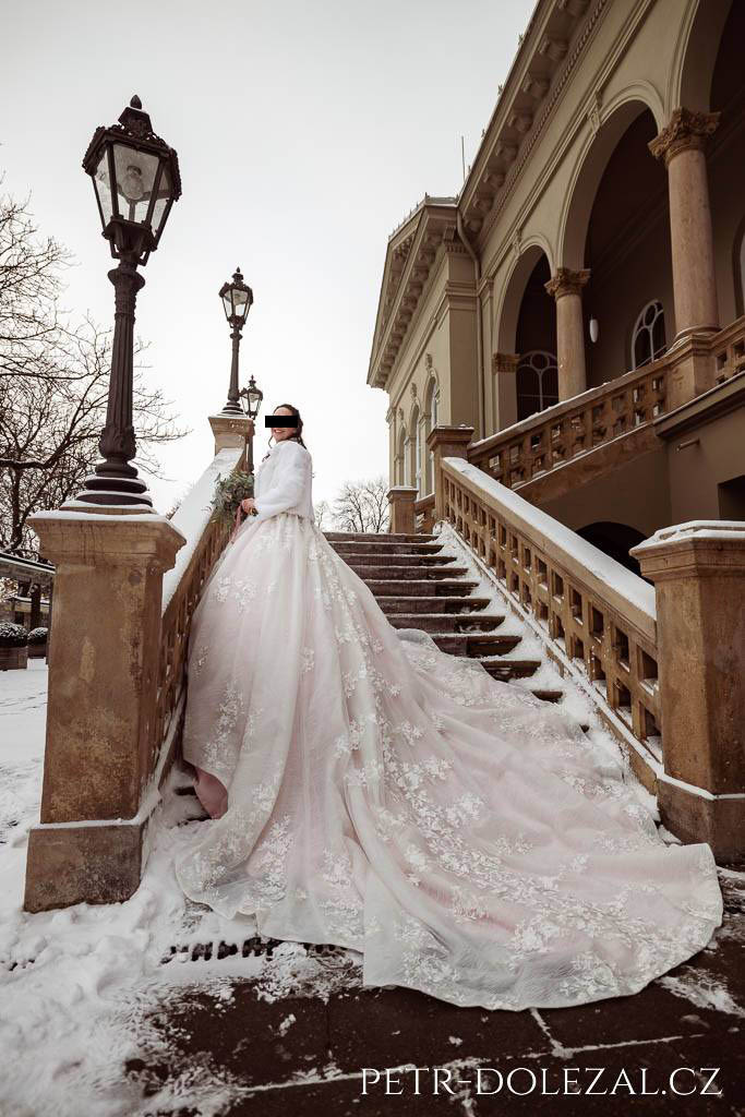 Nevěsta s dlouhými svatebními šaty na zasněženém schodišti Letenského zámečku