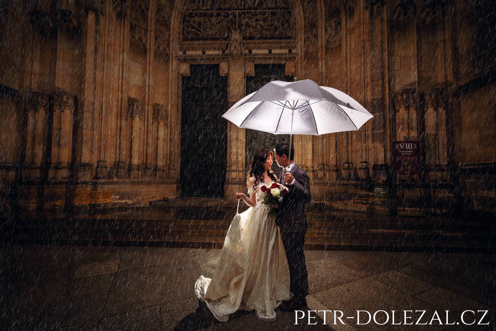 Nevěsta a ženich v dešti pod deštníkem před katedrálou na Pražském hradě
