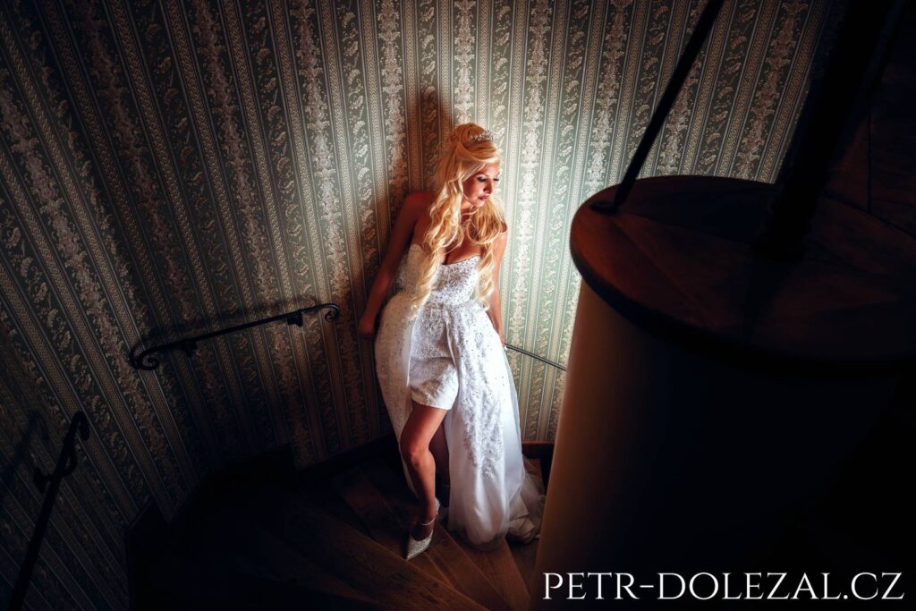 Bride posing at a wedding on a spiral staircase from a bird's eye view, looking to the right where the light is coming from
