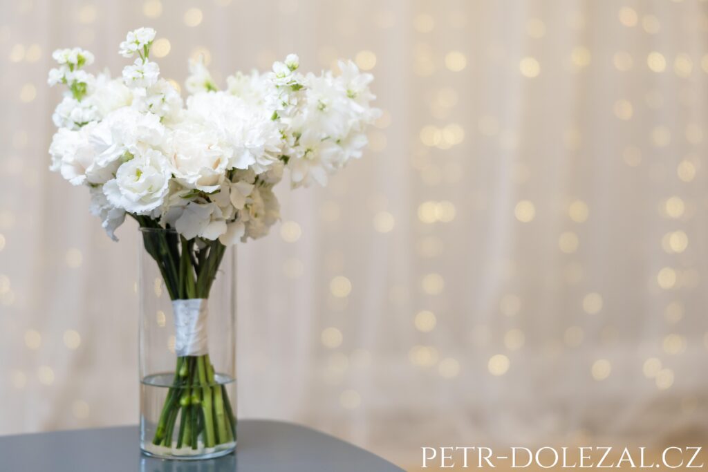 kytice nevěsty ve váze, v pozadí rozostřená světýlka