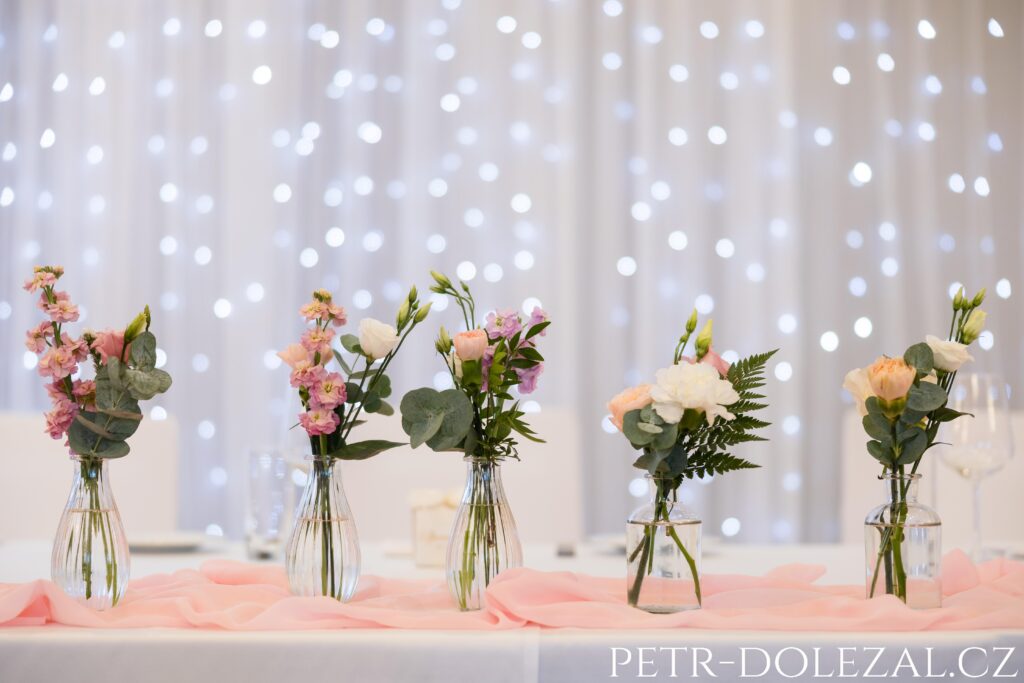 květinové dekorace na místě svatební hostiny, v pozadí rozostřená světýlka rozsvícené stěny