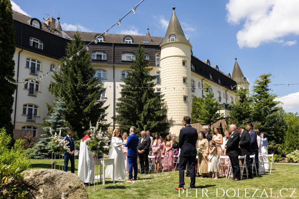 svatební obřad se všemi účastníky vyfocený zepředu, v pozadí hotel Sen Senohraby