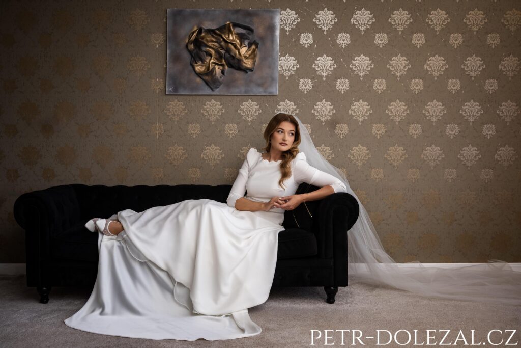 portrét nevěsty sedící na tmavé sedačce, na zdi tapety hotelového pokoje