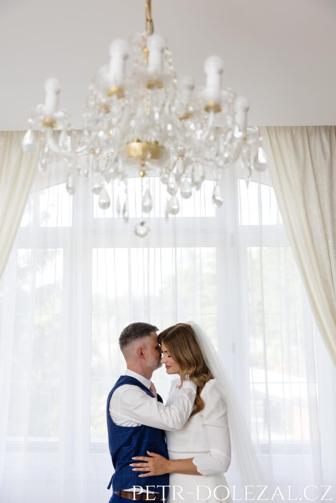 nevěsta se ženichem před velkým oknem se závěsy