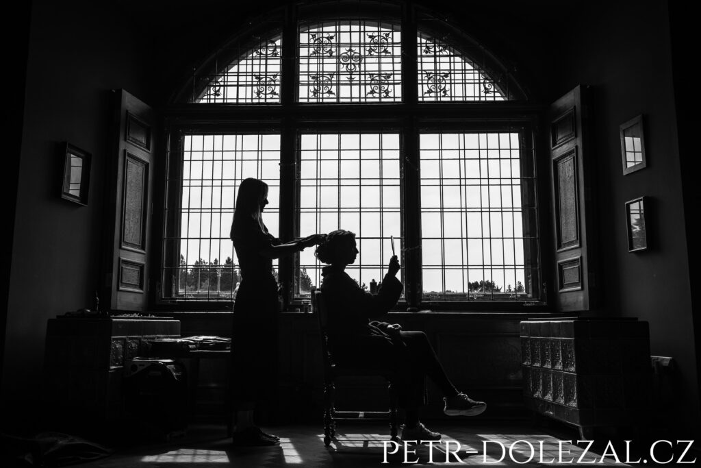 Černobílé foto z příprav nevěsty před velkým oknem Průhonického zámku