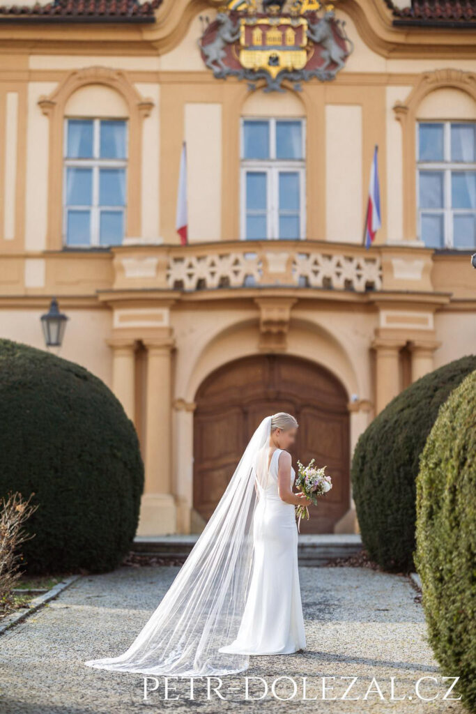 Nevěsta se závojem otočená zády, v pozadí zámek
